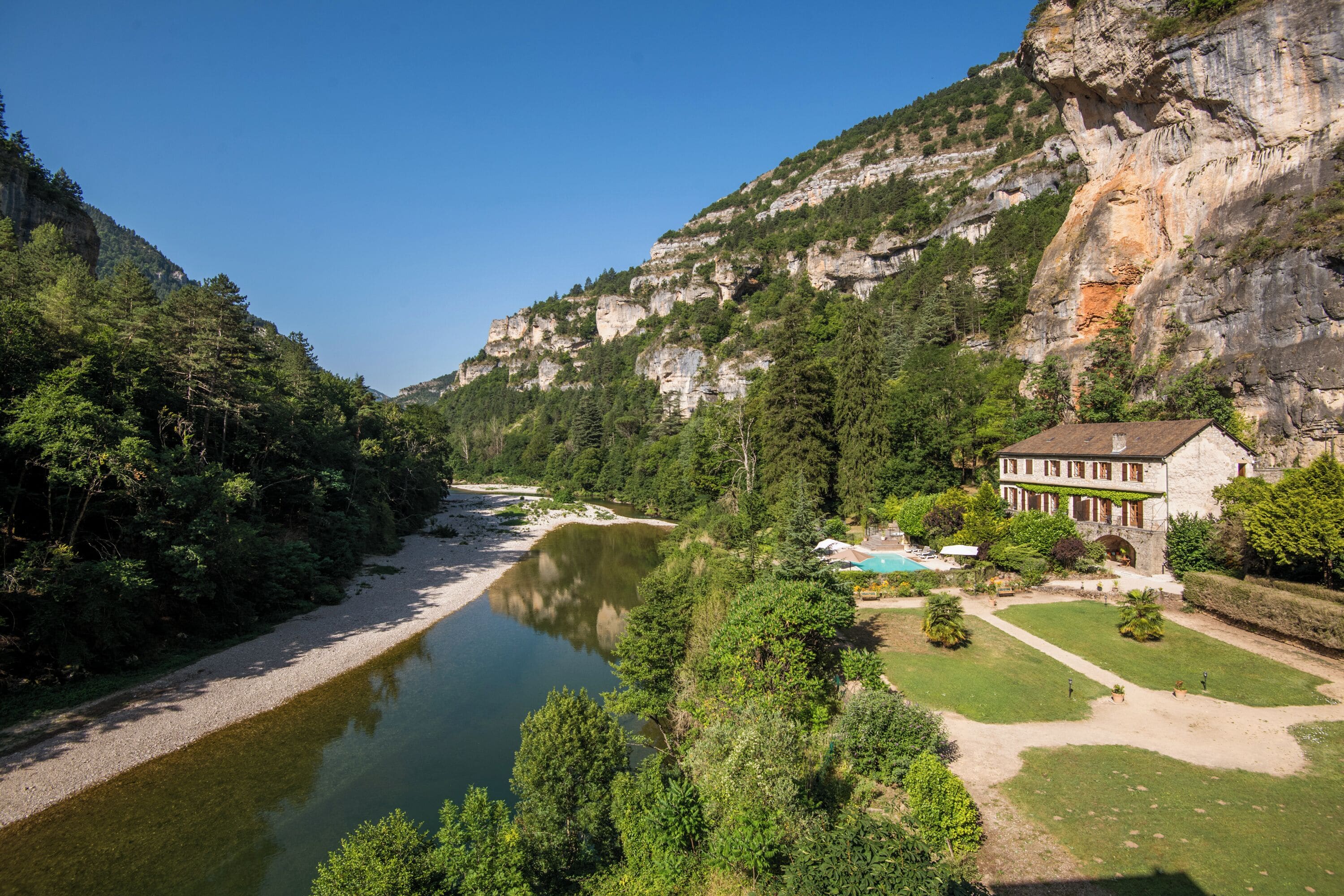 Ein Flussuferhotel mit Schwimmbad, umgeben von üppiger Vegetation und einer Felsklippe.
