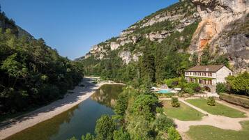 A riverside hotel with a swimming pool, surrounded by lush greenery and a rocky cliff.