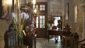 Un pasillo de paredes de piedra con un mostrador de recepción de madera, un candelabro y un suelo de baldosas.