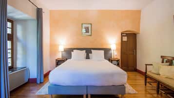 A hotel room with a large bed, two bedside lamps, a wooden bench, a door, and a framed picture on the wall.