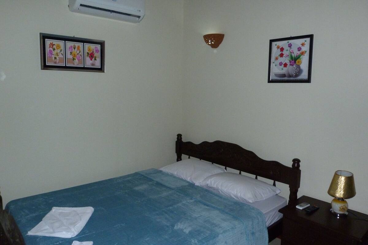 Une chambre à coucher comprenant un lit, une table de chevet, une lampe et des œuvres d’art accrochées au mur.