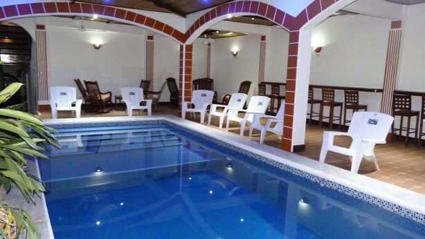 Une piscine intérieure avec des chaises blanches et un sol carrelé.
