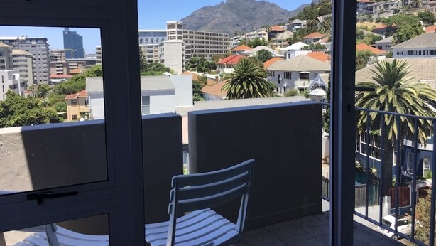 En balkon med en stol, udsigt over bybillede med bygninger og et bjerg.