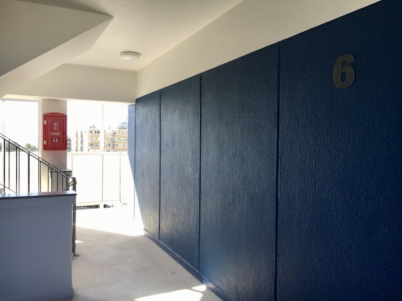 Um corredor com parede azul, um extintor de incêndio vermelho e o número 6 na parede.
