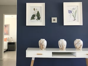 Ett rum med ett vitt konsolbord placerat mot en mörkblå vägg. På bordet står två inramade botaniska illustrationer och tre vaser i marmor.