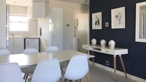 Et moderne køkken med hvide skabe, en indbygget opvaskemaskine og et spiseområde med et hvidt bord og stole.