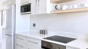 Et moderne køkken med hvide skabe, et rustfrit stål køleskab, en mikrobølgeovn, en vask og en sort bordplade.