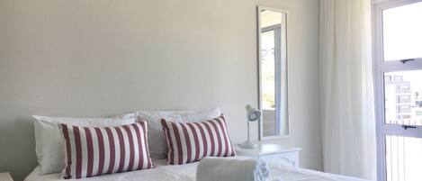 A neatly made bed with striped pillows, a bedside lamp, and a window with curtains.