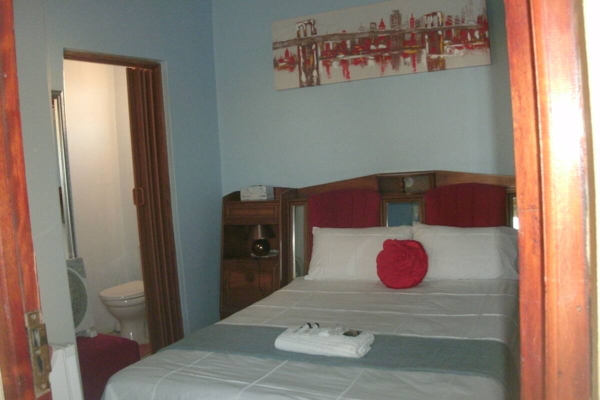 A hotel room with a bed, a wooden dresser, a mirror, and a painting on the wall.