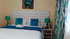 Una cama bien hecha con un cabecero capitonado, dos lámparas de noche y un cuadro decorativo encima.