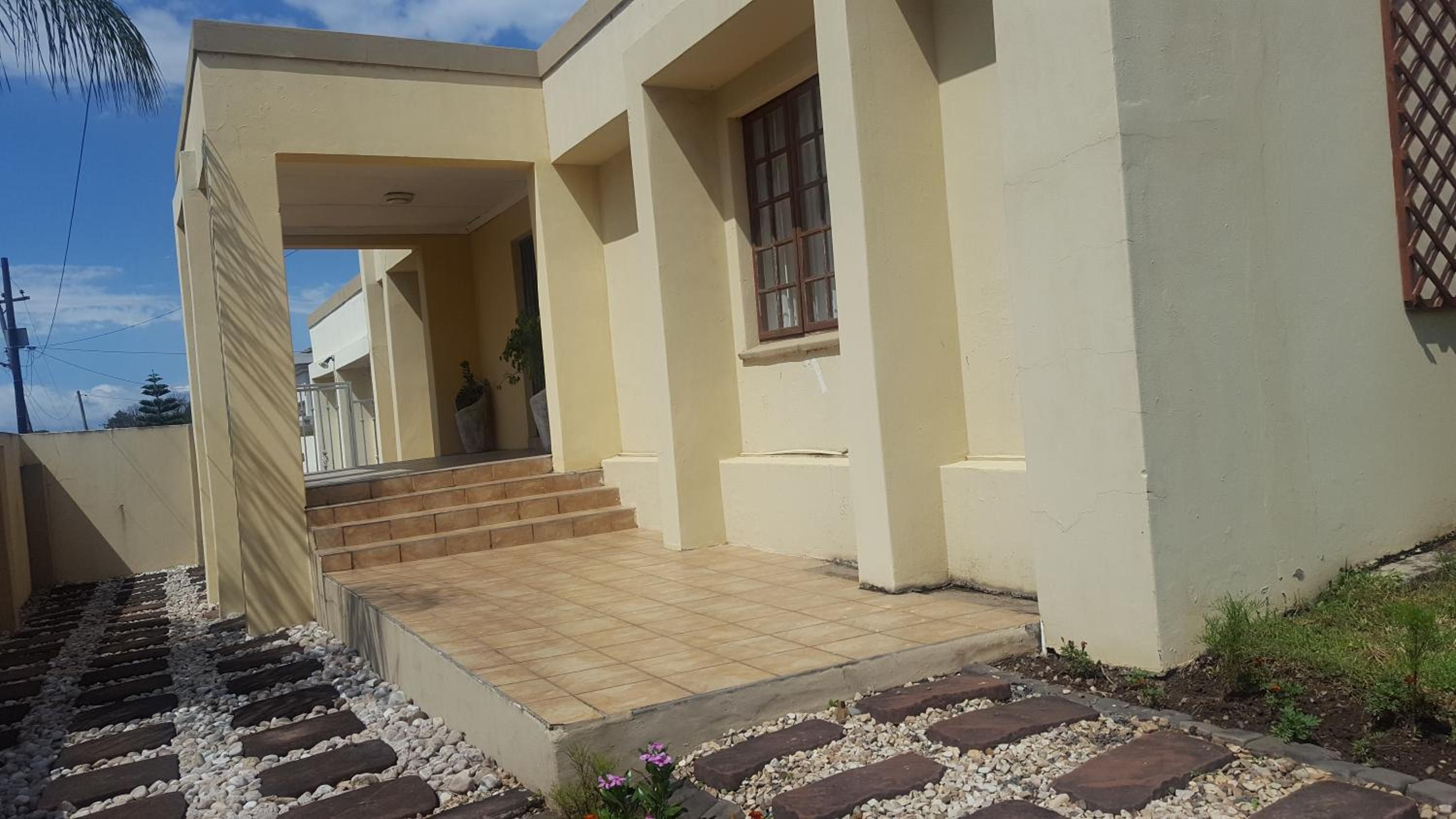 Una casa moderna con un porche cubierto, una escalera que conduce a la entrada y un jardín con piedras para caminar.