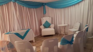 Una habitación con un sillón blanco, una mesita redonda y sillas con cintas azules.