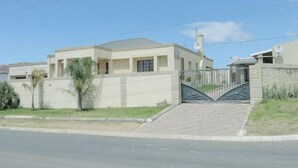 Una casa moderna de dos pisos con entrada protegida por un portón, techo plano y pequeño jardín delantero.