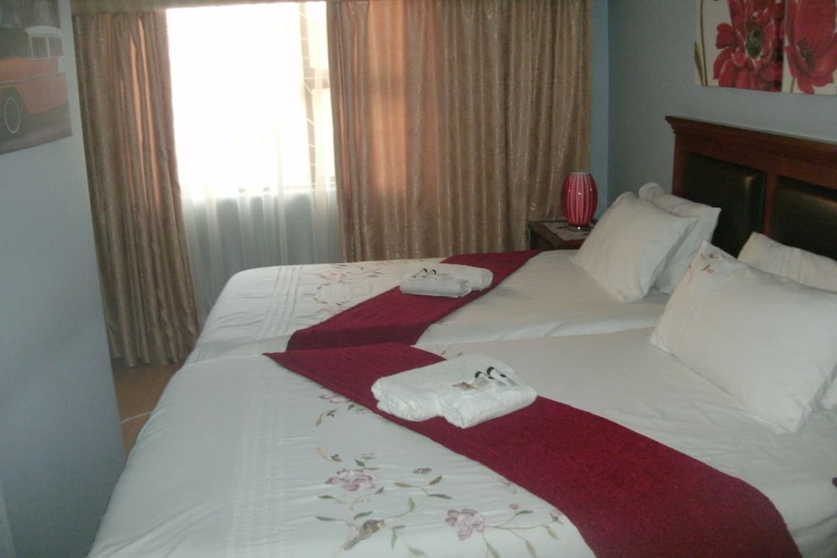 A hotel room with two beds, a red throw blanket, white pillows, and a floral bedspread.