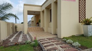 Un edificio moderno con entrada pavimentada, un pequeño jardín con adoquines y una palmera.