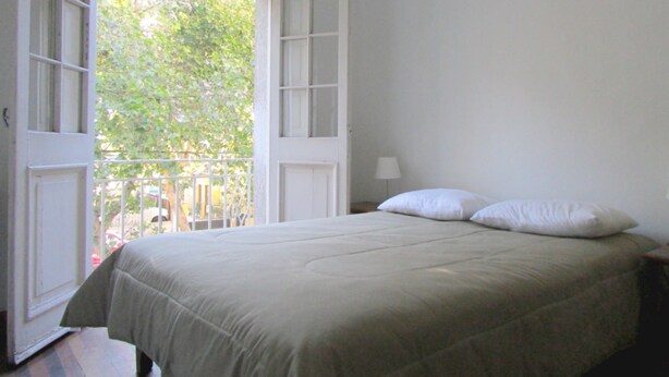 A bedroom with a bed, a nightstand, a lamp, and an open door leading to a balcony. - Casa Provence (Santiago)