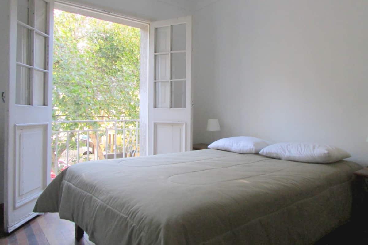 A bedroom with a bed, a nightstand, a lamp, and an open door leading to a balcony.