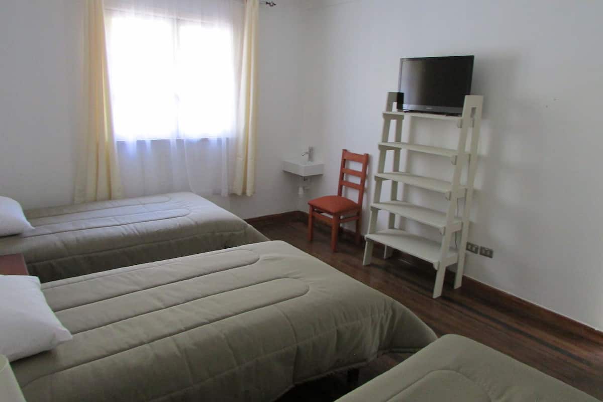 A room with two beds, a chair, a TV on a shelf, and a window with curtains.
