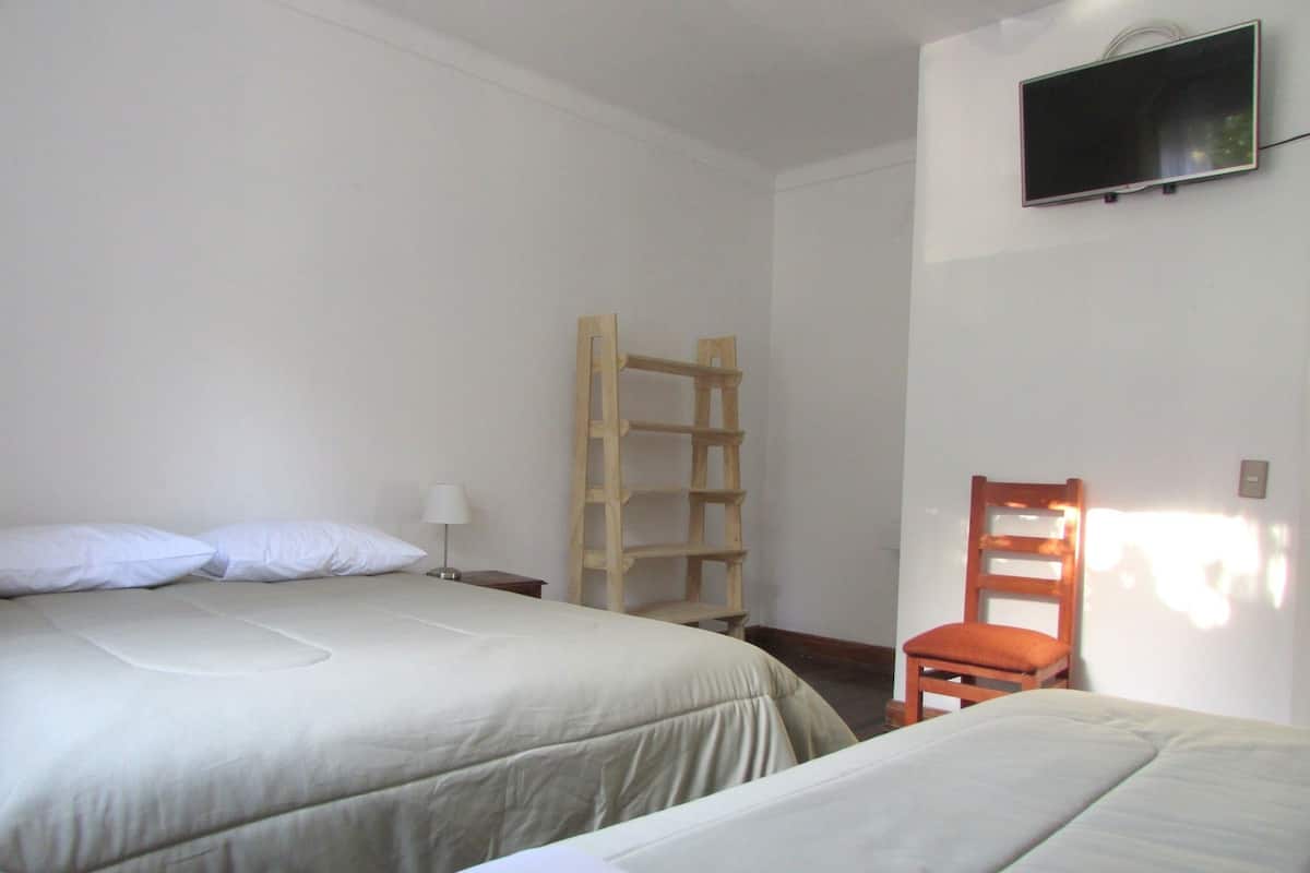 A room with two beds, a wooden ladder, a chair, and a TV mounted on the wall.