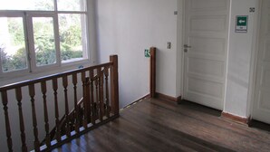 A hallway with a wooden staircase, a white door, and a window with a view of greenery. - Casa Provence (Santiago)