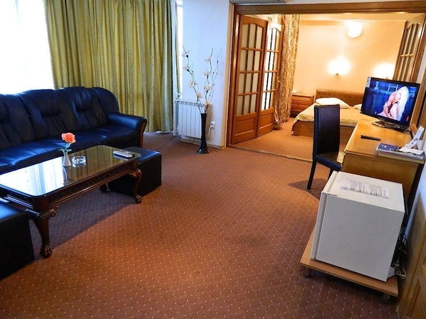 A hotel room with a sofa, a small table with a vase, a television, and a bed.