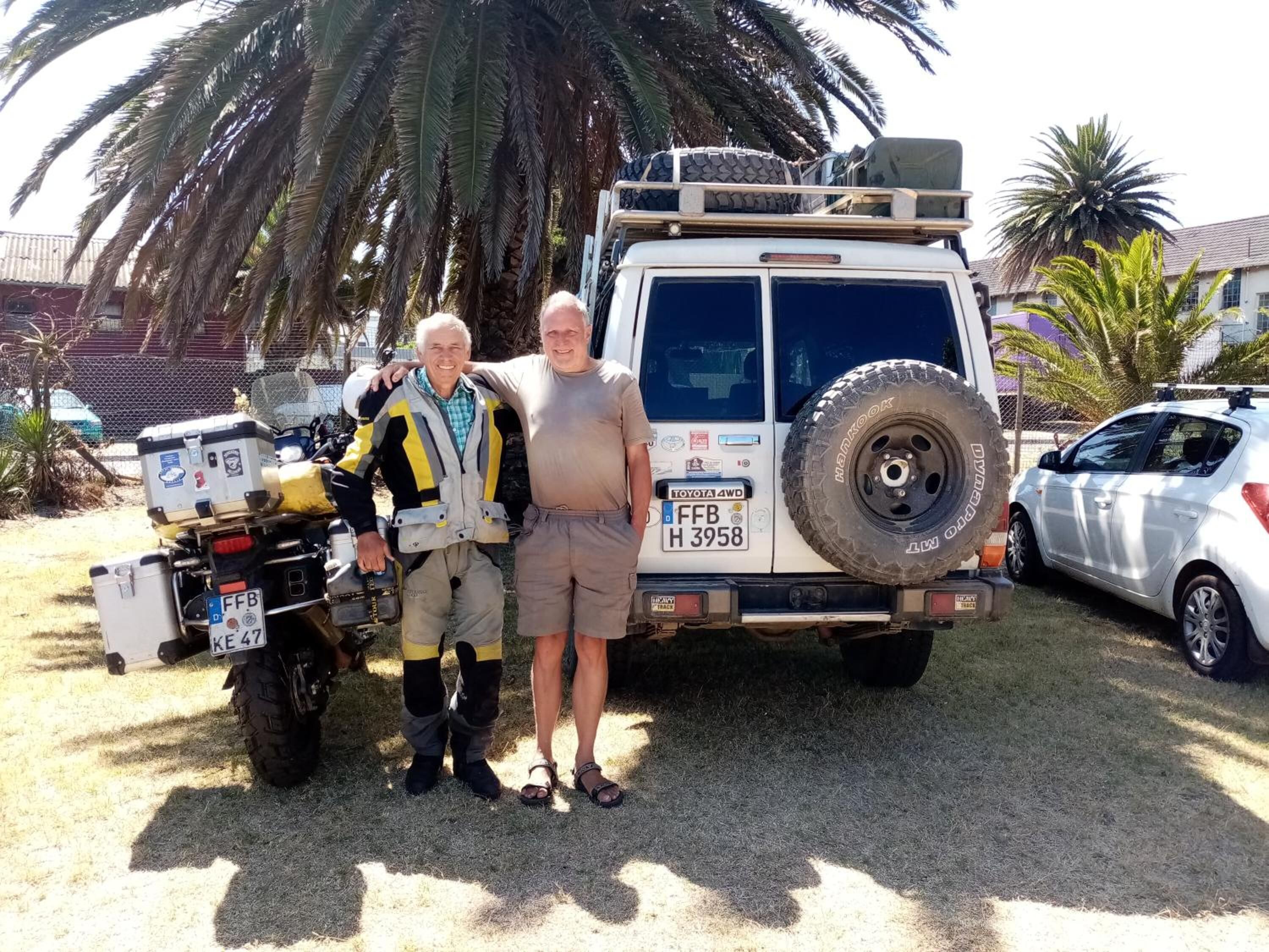 Two people standing in front of a white vehicle with a spare tire mounted on the back.