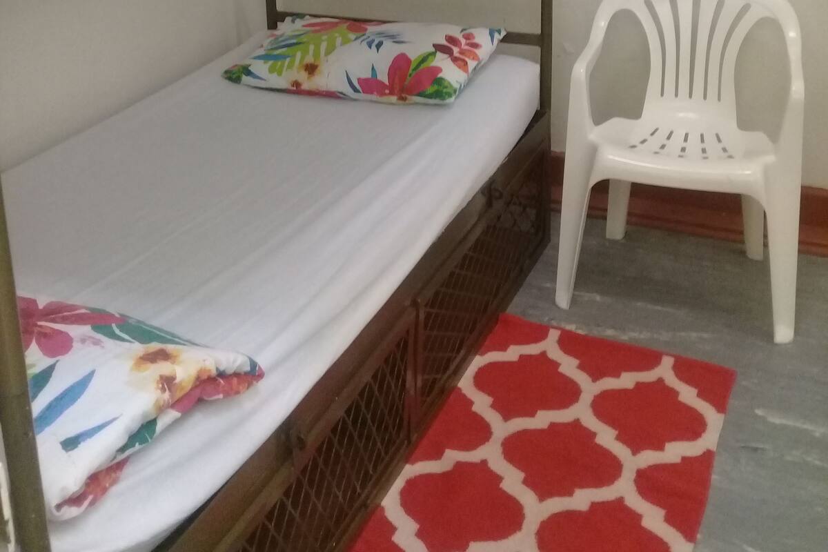 Un lit superposé avec un coussin à motifs floraux, une chaise en plastique blanche et un tapis rouge à motifs.