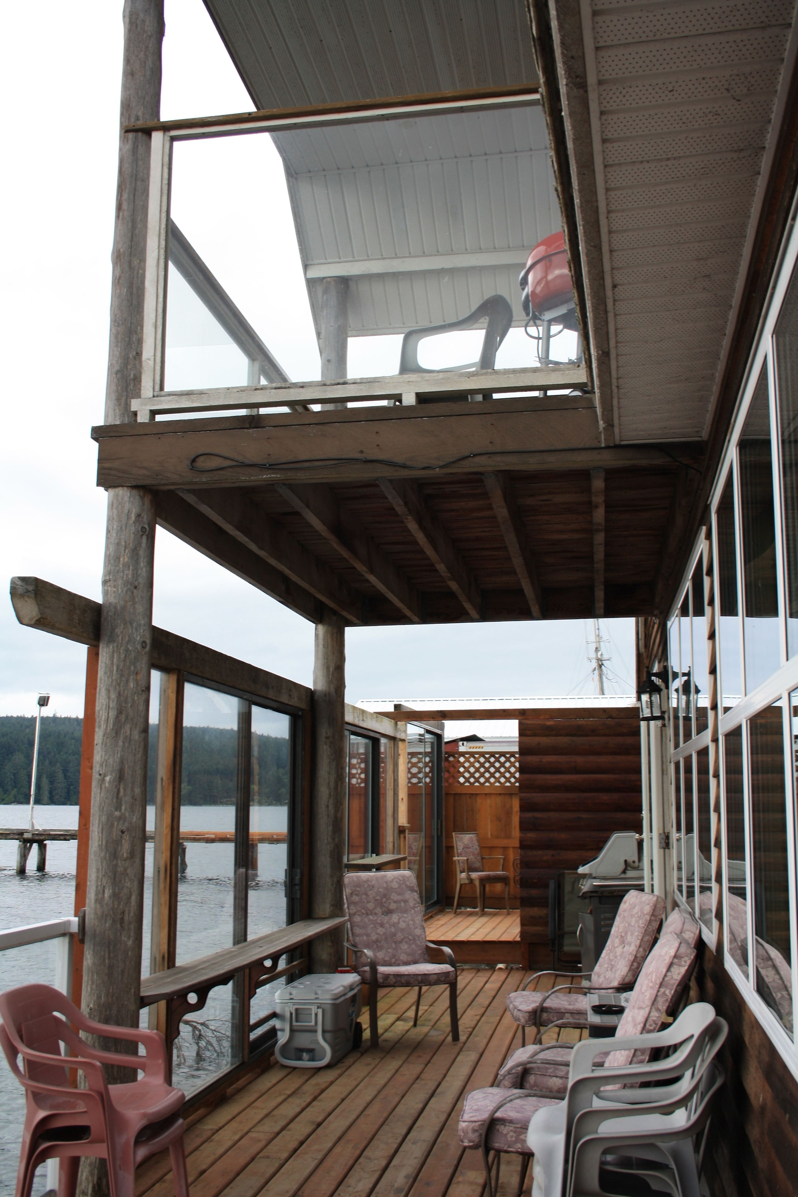 A wooden deck with chairs and a grill area, overlooking a body of water.