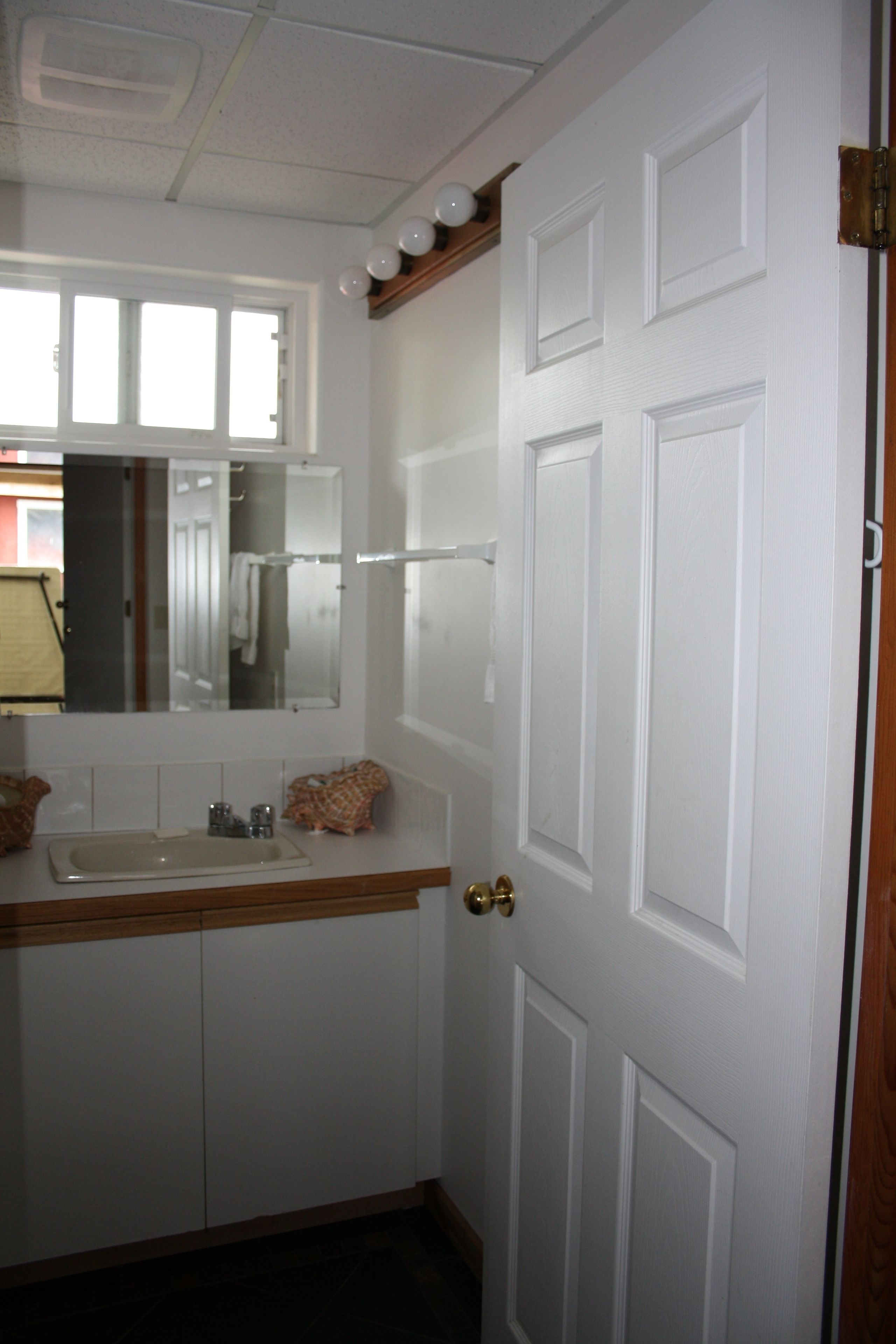 A bathroom with a white door, a mirror, a sink, and a towel rack.