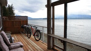 Une terrasse en bois avec deux vélos, un banc et une vue sur un lac, avec des montagnes en arrière-plan.