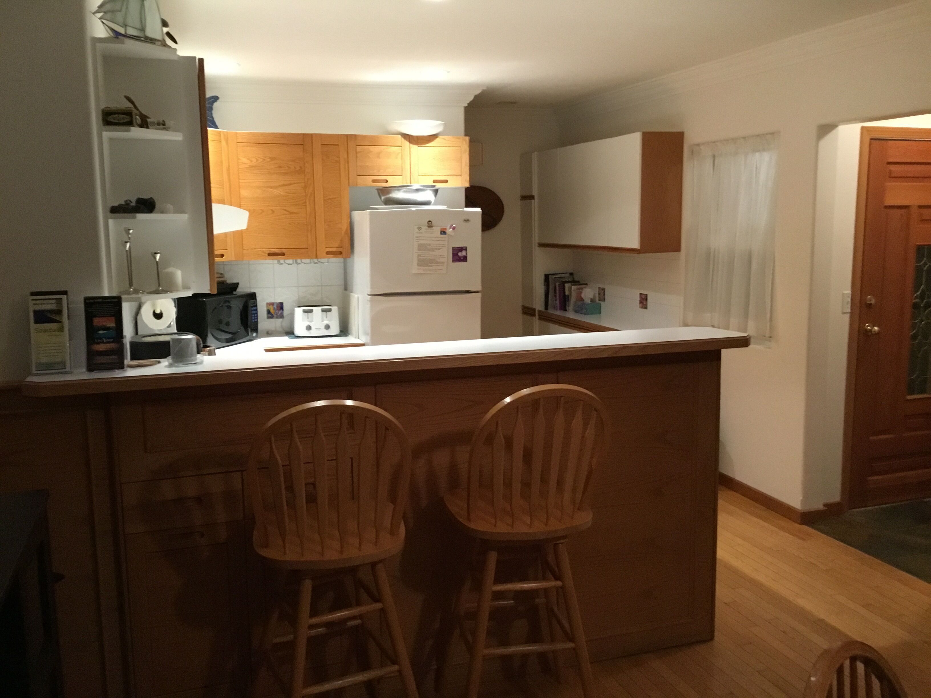 Une cuisine avec des meubles de rangement en bois, un réfrigérateur blanc, un four à micro-ondes et deux tabourets de bar en bois.