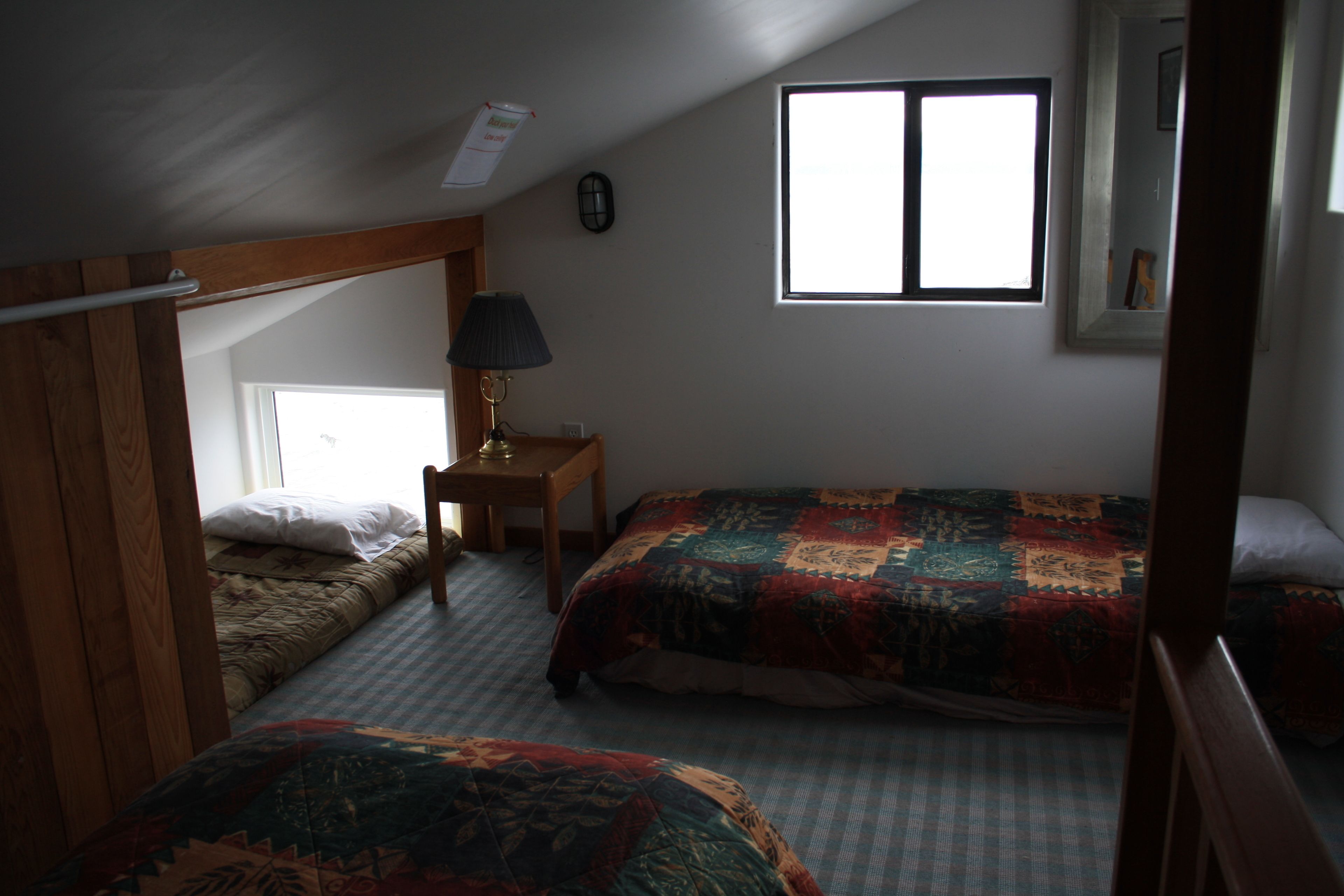 Ein Schlafzimmer mit zwei Betten, einem Fenster, einer Lampe und einem kleinen Tisch.