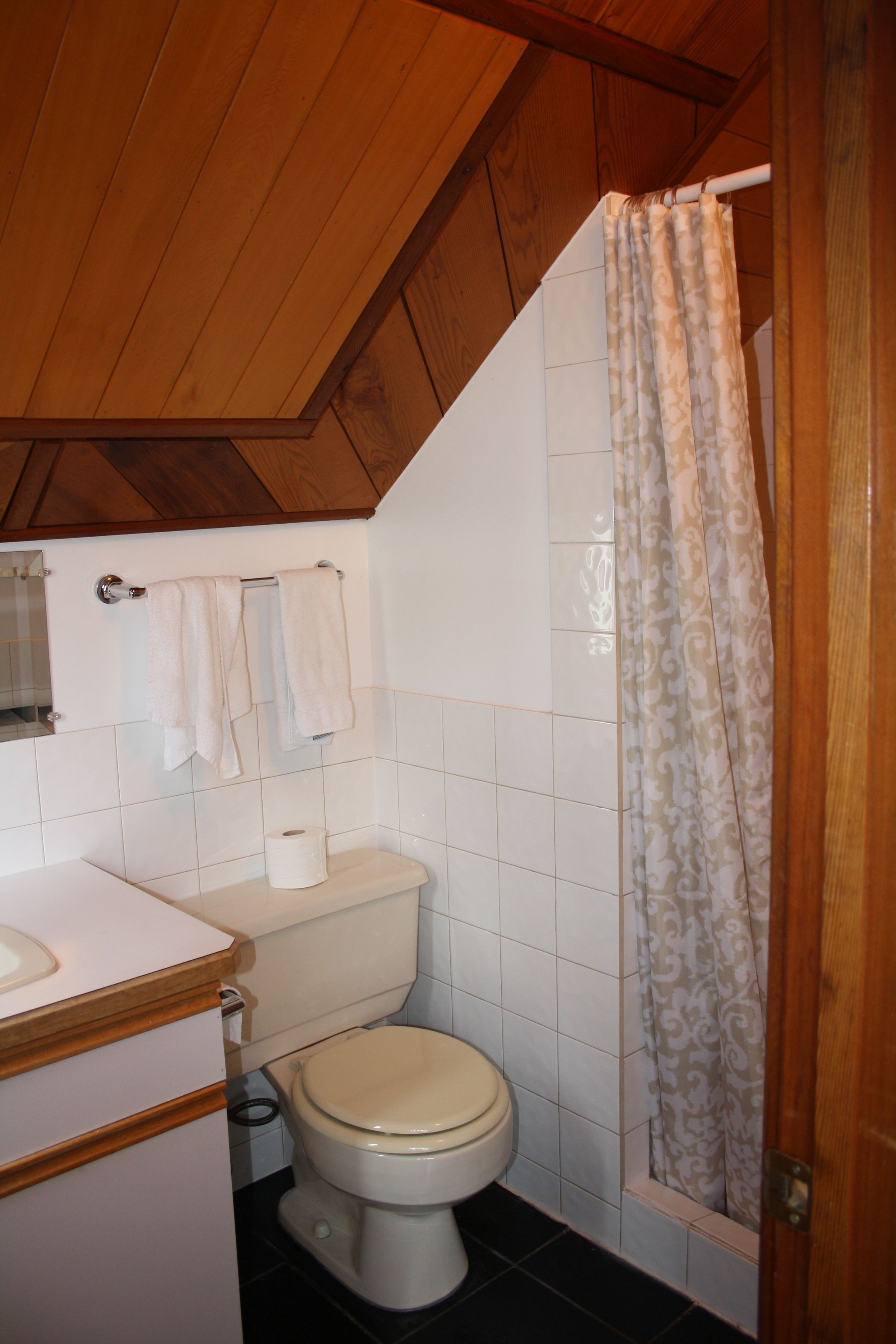 Un baño con techo de madera, un inodoro, un lavabo y una cortina de ducha.