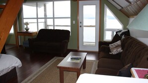 Un salon chaleureux avec un canapé marron, une table basse en bois et une vue sur la mer par une grande fenêtre.