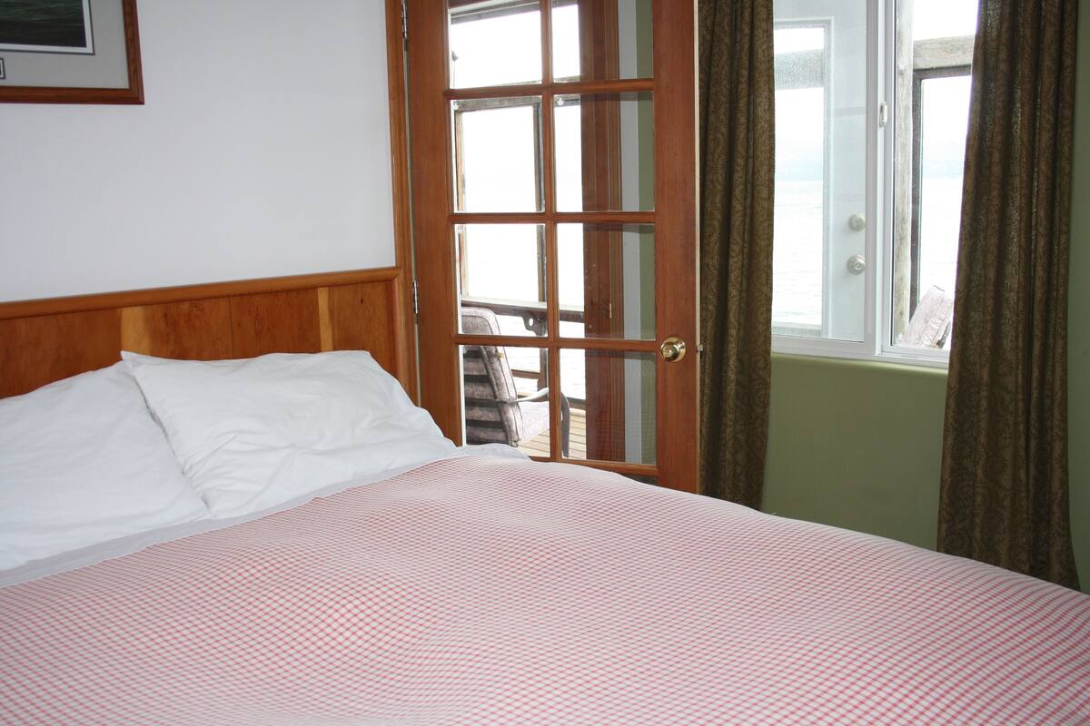 Habitación de hotel con cabecera de madera, cama con edredón a cuadros y ventana con cortinas, con vistas al exterior.
