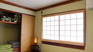 A traditional Japanese room with tatami flooring, a shoji screen window, and a storage cabinet with cushions. - Kumano House (Kyoto)