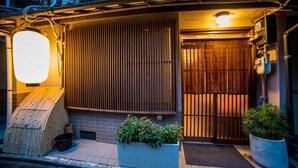 A traditional Japanese house with a wooden gate, a tiled entrance, and a small garden area with plants. - Kumano House (Kyoto)