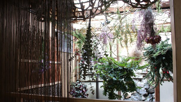 A traditional Japanese-style room with tatami flooring, a shoji screen, and a hanging garden with various plants and flowers. - Kumano House (Kyoto)