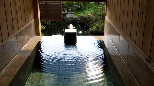 Un onsen japonés tradicional con vistas a un paisaje montañoso a través de una celosía de madera.