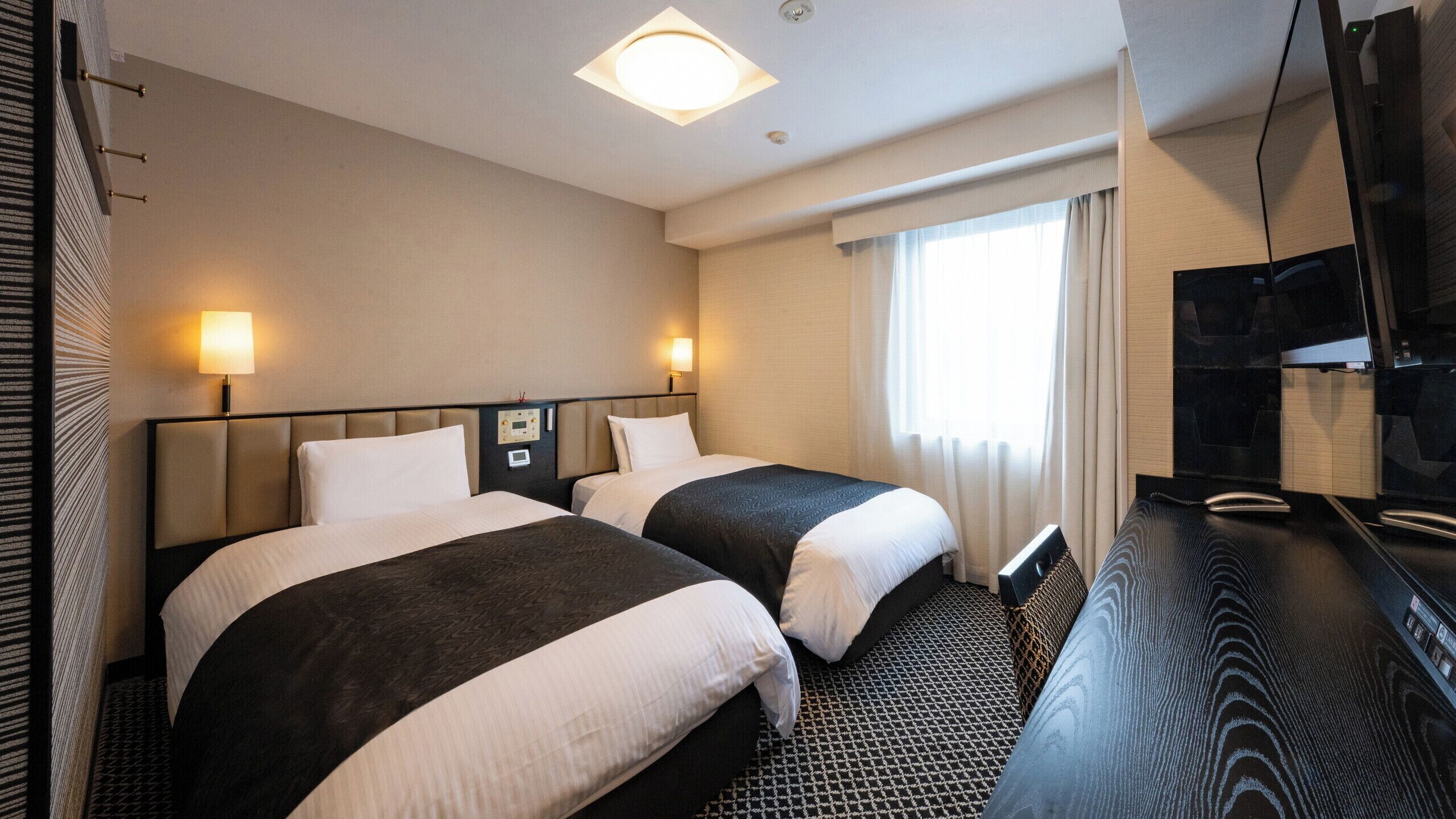 Hotelkamer met twee bedden, een flatscreen televisie, een bedieningspaneel en een raam met gordijnen.