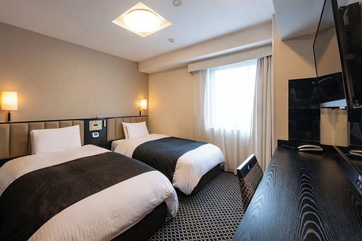 Hotelkamer met twee bedden, een flatscreen televisie, een bedieningspaneel en een raam met gordijnen.
