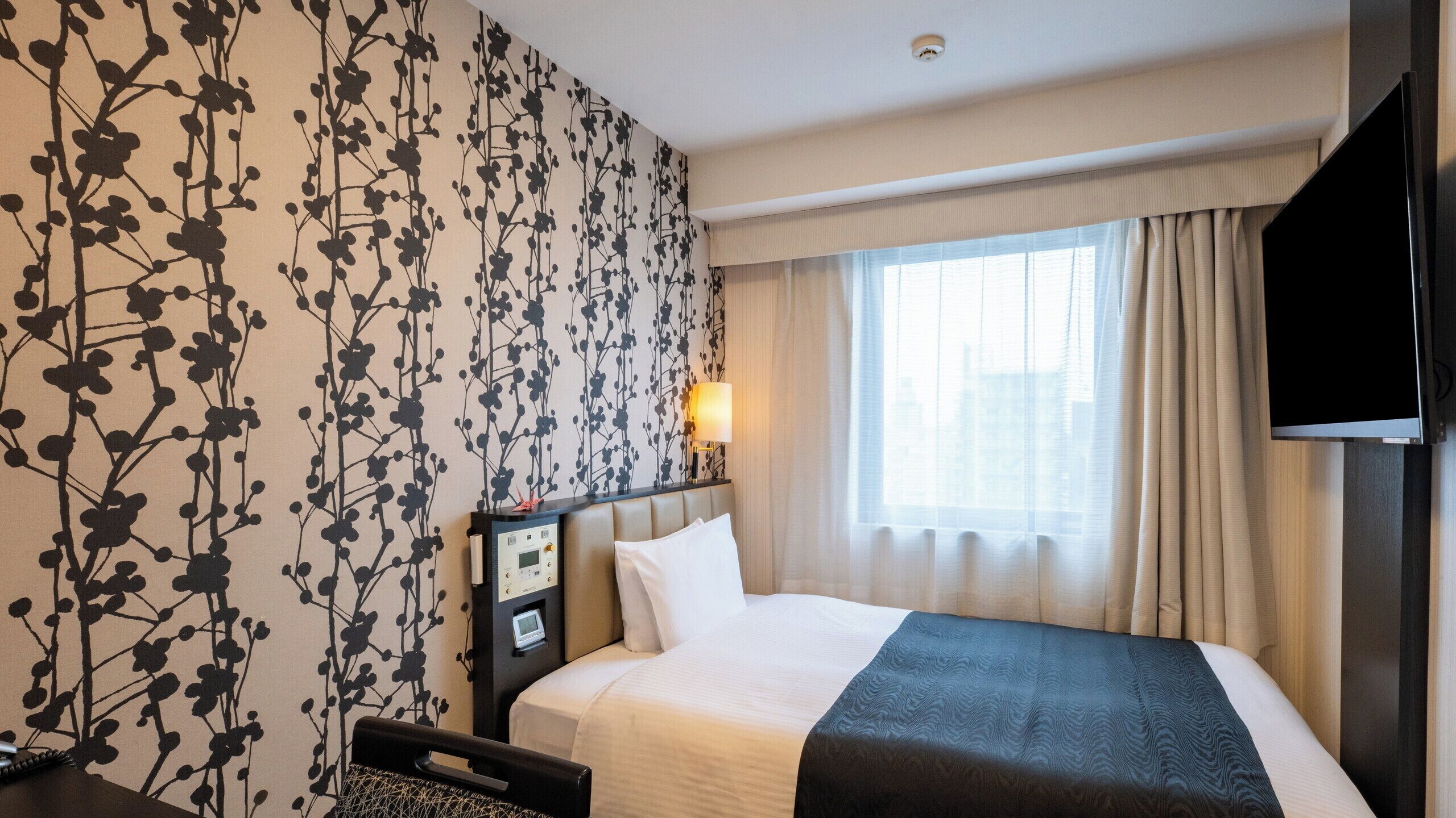 Een hotelkamer met een bed, nachtkastje met lamp, televisie en raam met gordijnen.