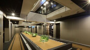 Un hall d’hôtel moderne doté d’une plateforme centrale en bois, de plusieurs ascenseurs et d’un plafond haut avec des puits de lumière.