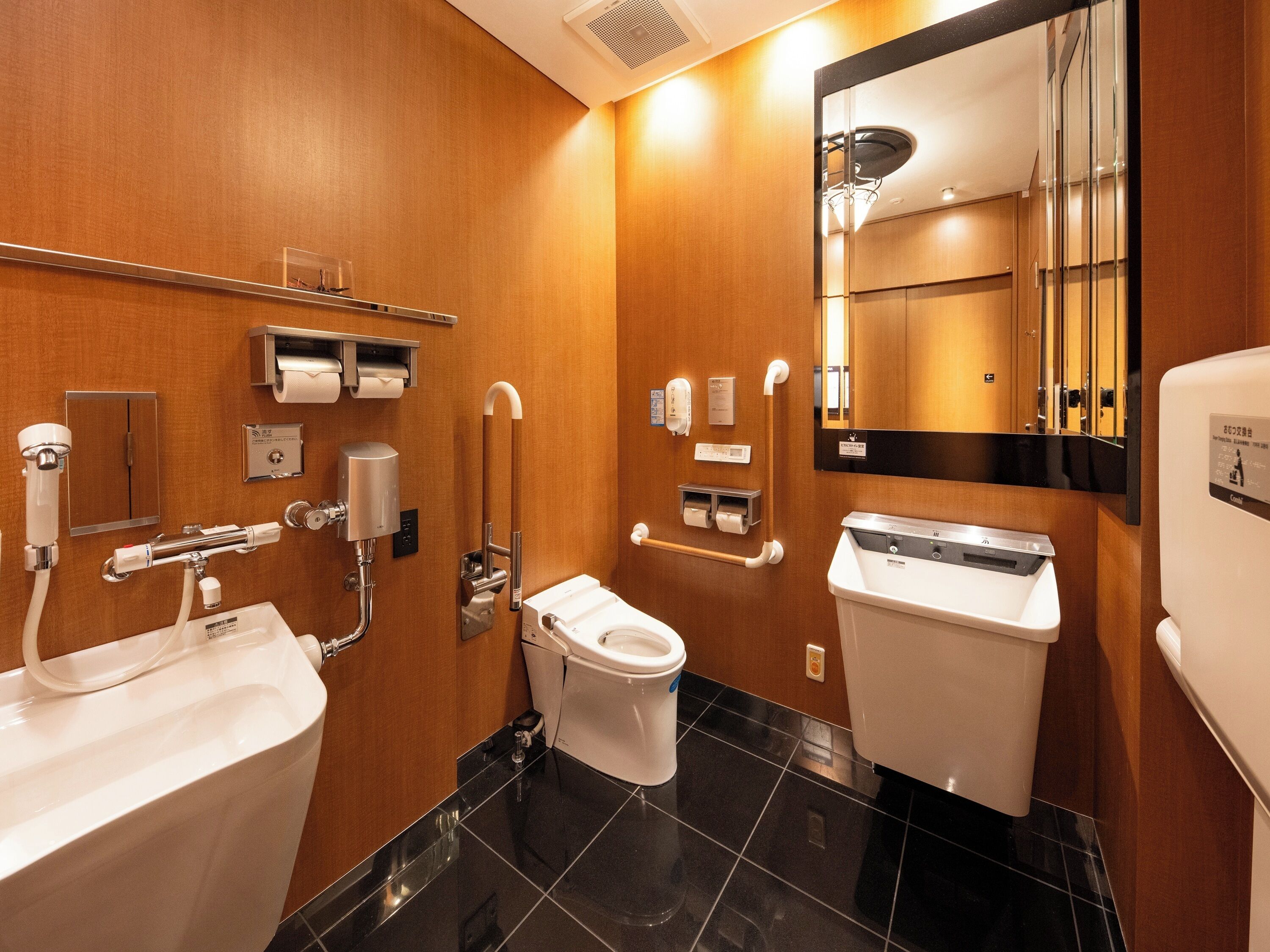 A modern bathroom with a toilet, bidet, and sink, equipped with accessibility features like grab bars and a handrail.