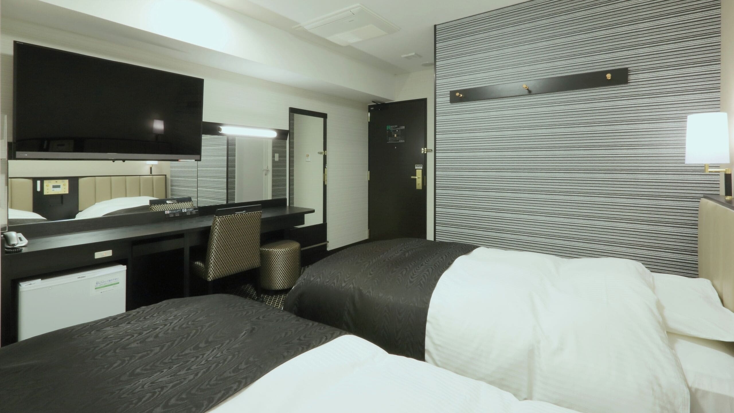 Ein Hotelzimmer mit Bett, Schreibtisch, Stuhl, Spiegel und Wand mit Streifenmuster.