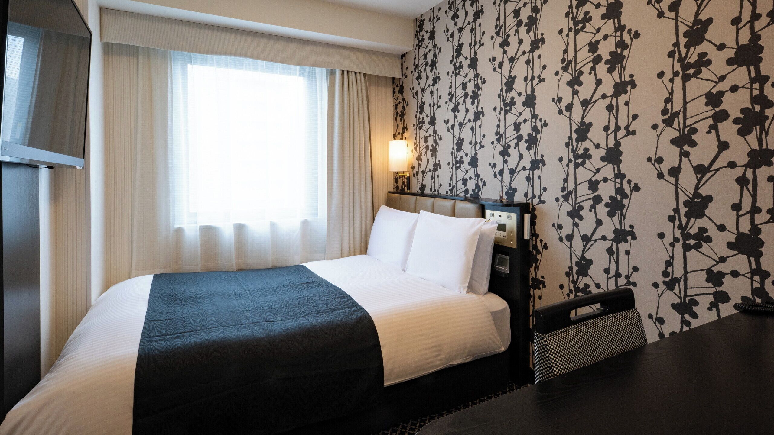 Een hotelkamer met een bed, een televisie, een nachtkastje en een muur met een bloemenprint.