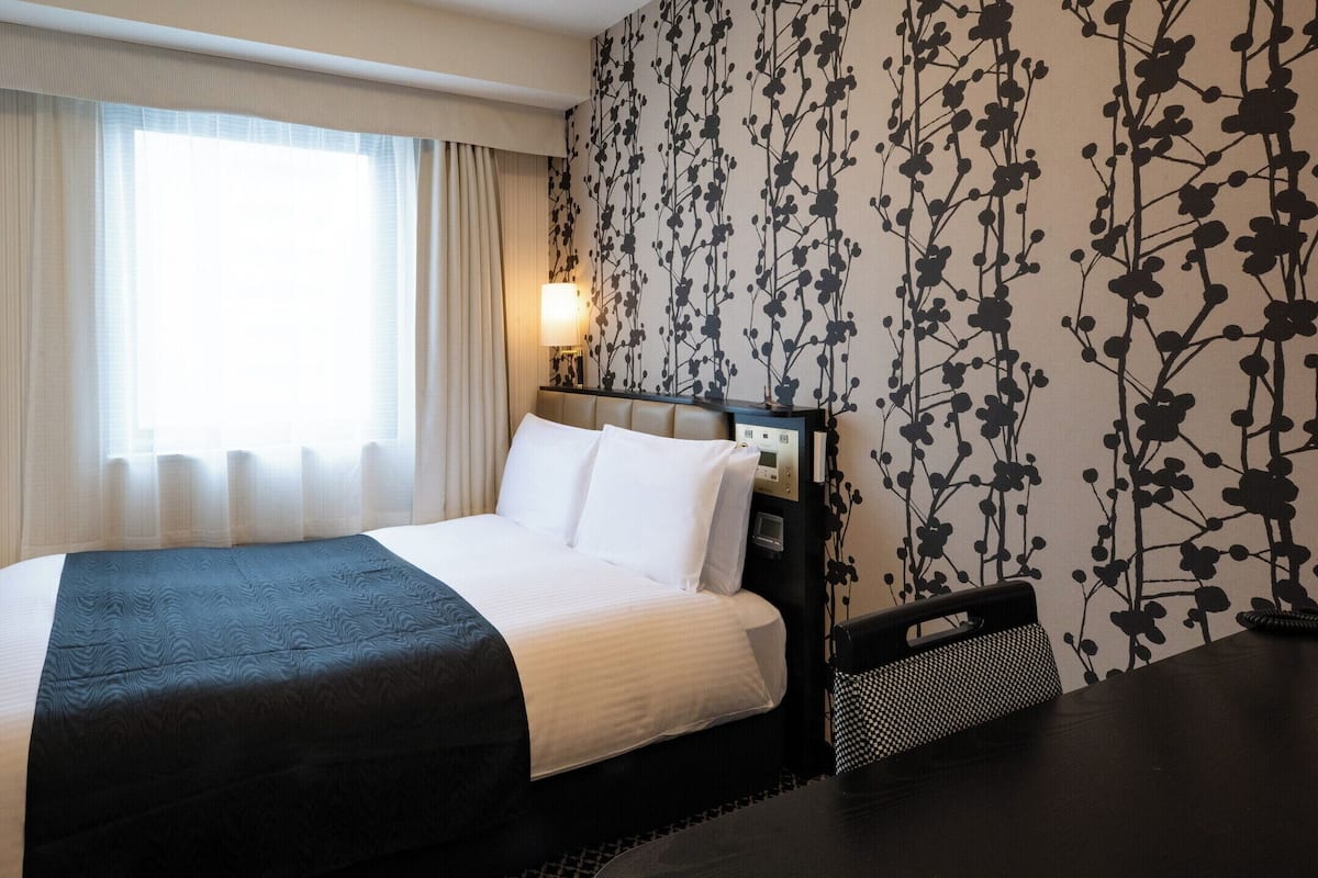 Una habitación de hotel con cama, televisión, mesita de noche y un muro con estampado floral.