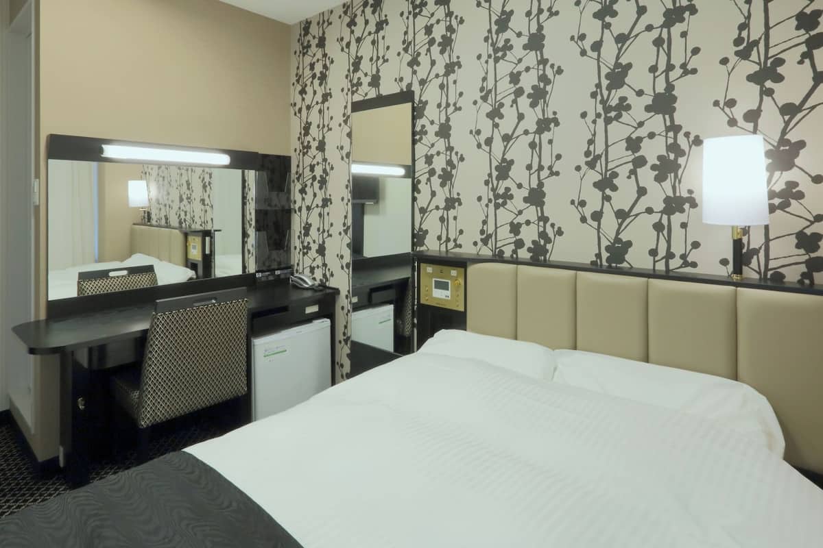 Habitación de hotel con cama, escritorio con computadora, espejo y pared con estampado floral.