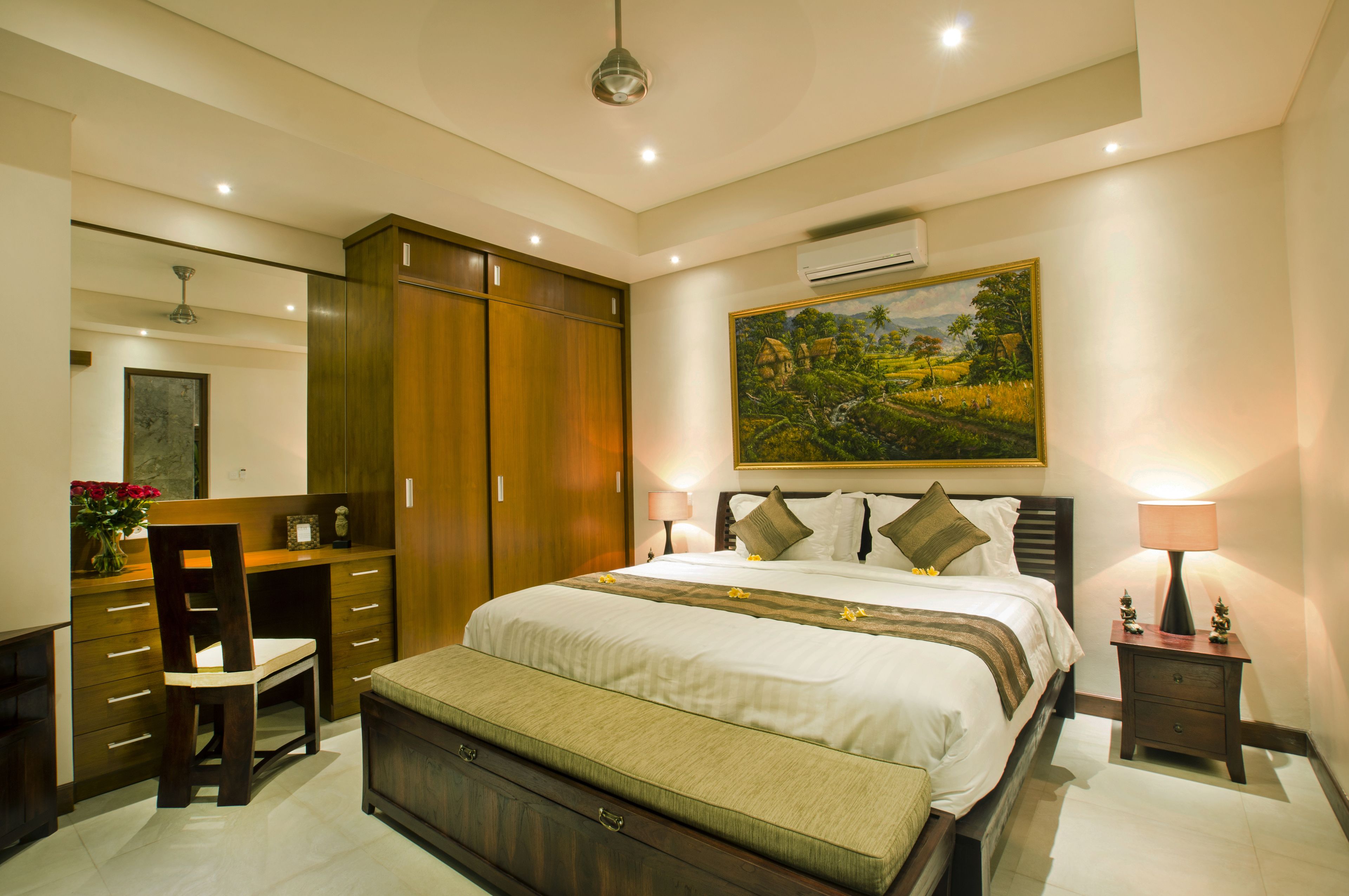A bedroom with a large bed, a desk, a chair, a wardrobe, and a painting on the wall.