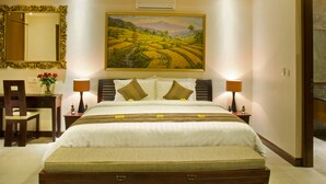 A bedroom with a large bed, a ceiling fan, a painting, and a desk with a chair. - The Oasis Retreat Seminyak (Seminyak)